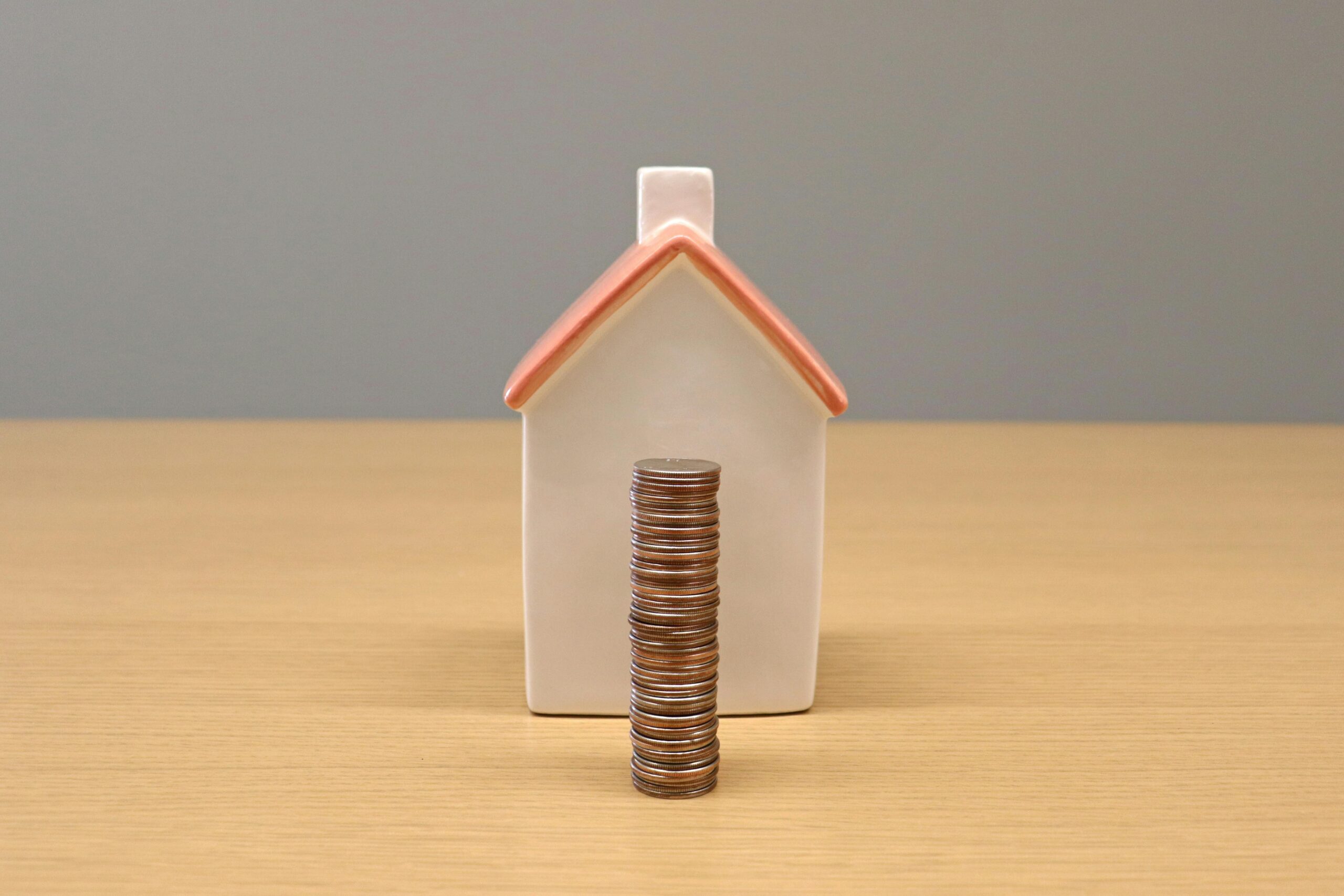 A conceptual still life image of stacked coins in front of a porcelain house, symbolizing savings and investment.